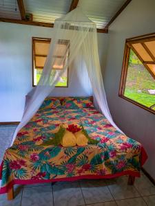 乌图罗阿Te Fare Manulani的带两扇窗户的客房内的一张带五颜六色棉被的床