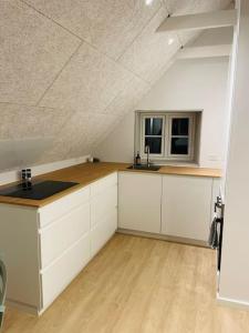 锡尔克堡Lejlighed i naturskønt område的阁楼厨房配有白色橱柜和窗户。