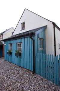 福里斯Driftwood Cottage, Findhorn Village的蓝色的建筑,设有两扇窗户和栅栏