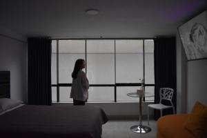 瓦努科Hotel Demetria的站在卧室里,看着窗外的女人