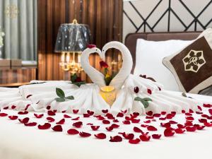 荣市Cửa Đông Luxury Hotel的两个天鹅坐在床上,上面有玫瑰花