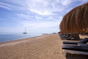 赫尔格达Ancient Sands Golf Resort and Residences的海滩上设有椅子和草伞,海洋