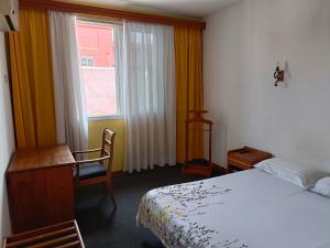 塔那那利佛Aina Hôtel的一间卧室配有一张床、一张书桌和一个窗户。