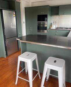 汉密尔顿CBD Apartment, River View的厨房配有绿色橱柜和2张白色凳子