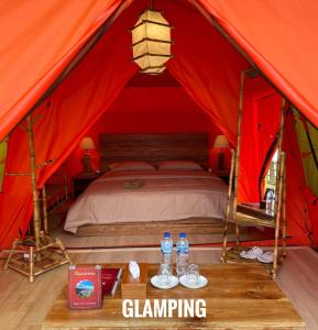 KejajarBagas Luxury Camp的红色帐篷内的一张床位,桌子上装有水瓶