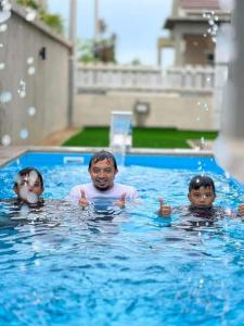 Guar ChempedakEl Manzil Homestay with Pool的一名男子和两名儿童在游泳池游泳