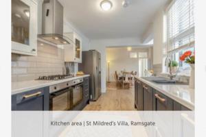 拉姆斯盖特St Mildreds Villa, Ramsgate Royal Harbour, Kent的一间设有蓝色橱柜的厨房和一间带用餐室的厨房