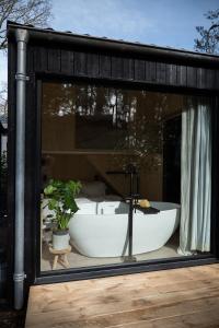 宁斯佩特Vague Luxurious Tiny House Luxe Wellness, Spa Bad,Beamer, Veluwe的浴缸坐在玻璃窗内