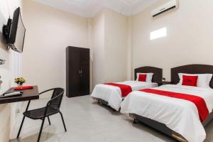棉兰RedDoorz At Ralica Grand Palladium Medan的一间卧室配有两张床、一张桌子和一台电视。