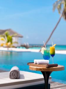 弗里德胡NOOE Maldives Kunaavashi的一张桌子,旁边是游泳池,旁边是饮料和毛巾