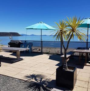 WaitahanuiWaitahanui Lodge的海滩上的一组野餐桌和遮阳伞