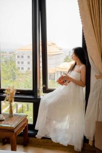 岘港SeaColor Beachstay Danang Hotel by Haviland的穿着婚纱的女人,从窗户望出去