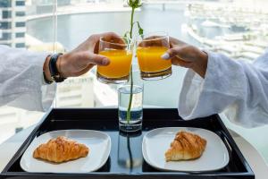 迪拜Unlock J One Downtown Dubai的两人把橙汁和糕点杯放在托盘上