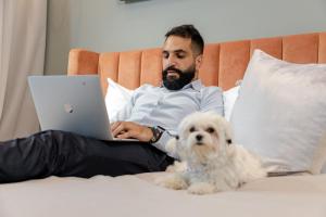 迪拜Unlock J One Downtown Dubai的坐在床上的男人,手提电脑和狗
