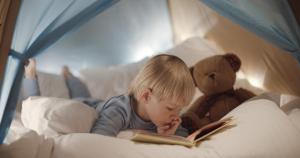 特拉基太浩湖丽思卡尔顿酒店的躺在床上的小男孩用泰迪熊看书