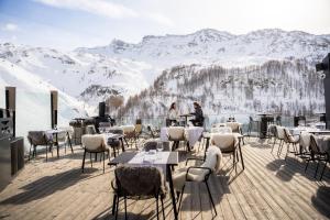 布勒伊-切尔维尼亚Bergman Mountain Hotel的一间在甲板上设有桌椅的餐厅,甲板上拥有积雪覆盖的山脉