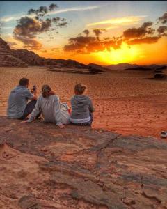 瓦迪拉姆Enad desert camp的三人坐在海滩上欣赏日落