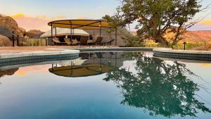 KhorixasTwyfelfontein Adventure Camp的一个带桌椅和树的游泳池