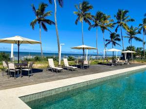 伊列乌斯Kalug - Duplex PÉ NA AREIA com 4 suítes, piscina e churrasqueira privativa na Praia do Sul! Perfeito para família - Wifi 300mb!的一个带桌椅和遮阳伞的游泳池