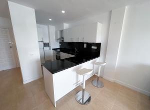 拉萨维纳Turquesa & Ambar Apartments Formentera的白色的厨房,配有黑色的柜台和凳子