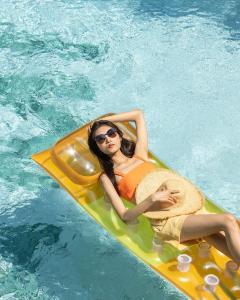 曼谷Miami Hotel Bangkok - SHA Plus的躺在游泳池里的木筏上的女人