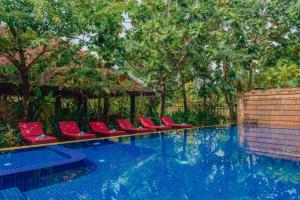 暹粒Pandora Suite D'Angkor的一个带红色椅子和树木的游泳池