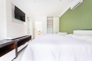瓜鲁雅Suites Guarujá Pernambuco的白色卧室设有一张大床和一台平面电视。
