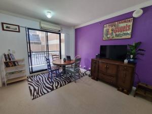 珀斯Little Monica Apartment- Spacious, Affordable & Central的客厅配有桌子、电视和紫色墙壁。