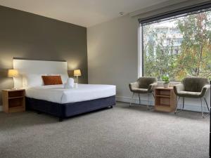 墨尔本墨尔本大都会酒店的一间卧室配有一张床、两把椅子和一个窗户