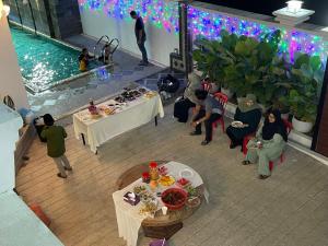 Pasir MasAainaa Villa Homestay的一群人坐在桌旁,坐在一个带游泳池的房间