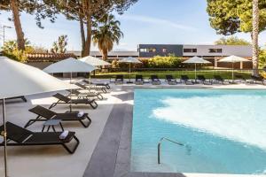 佩皮尼昂Holiday Inn Perpignan, an IHG Hotel的一座带椅子和遮阳伞的游泳池位于一座建筑旁边