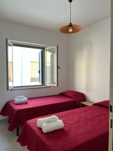 拉卡勒塔La casa di Tonia的客房设有两张带红色床单的床和窗户。