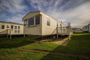 亨斯坦顿Lovely Caravan With Decking At Manor Park Nearby Hunstanton Beach Ref 23017t的草坪上的小黄色房子,带门廊