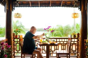 会安Eco Wooden villa Hoi An的坐在餐桌上吃一盘食物的人