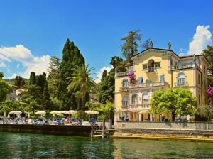 加尔多内-里维耶拉Hotel Monte Baldo e Villa Acquarone的河边一座带椅子和遮阳伞的建筑