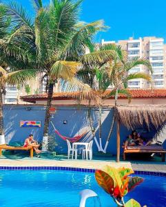 伊塔尼亚恩Hostel Praia Centro Itanhaém的一座棕榈树游泳池,人们坐在椅子上
