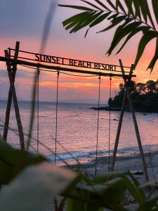 沙璜Sunset Beach Resort Weh的海滩上的日落,带有日落度假区读书的标志