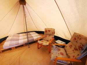 GräsmarkVolledig ingerichte tent op natuurcamping的一间卧室配有一个带一张床和两把椅子的帐篷