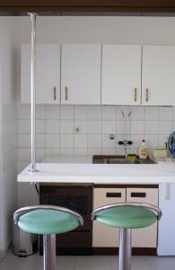 KikindaMileva apartman的厨房配有白色橱柜和2张绿色酒吧凳