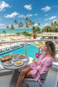 马拉戈日Maragogi Brisa Exclusive Hotel的坐在餐桌旁的女人,在度假村的阳台上享用早餐