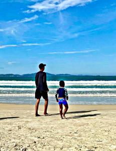 卡波布里奥FLAT / APARTAMENTO NA PRAIA DO FORTE的海滩上散步的男人和孩子