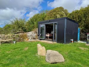 赫尔斯顿Rhubarb Hut, set in the beautiful Cornish Countryside的草地上一块石头的黑棚