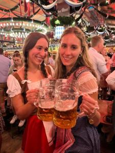 慕尼黑Festanation Oktoberfest Camp #2的两个女人在酒吧里拿着杯啤酒