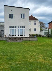 Solrig og moderne villalejlighed tæt på midtbyen的一座白色的大房子,前面有一片绿色草坪