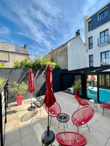 贝诺代Le Cornouaille Hotel & Spa的一个带红色椅子和遮阳伞的庭院和一个游泳池