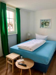 维特Pension "Strandhotel"的一间卧室配有蓝色的床、一张桌子和一个窗户。