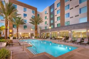 霍桑TownePlace Suites by Marriott Los Angeles LAX/Hawthorne的一座酒店游泳池,在一座建筑前,设有椅子和棕榈树