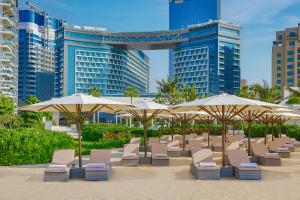 迪拜NH Collection Dubai The Palm的建筑前的海滩,配有椅子和遮阳伞
