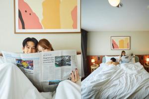 曼谷Arck Hotel的两个人躺在床上看报纸
