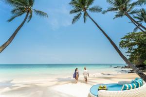 湄南海滩Four Seasons Resort Koh Samui的两对夫妇在棕榈树海滩上散步